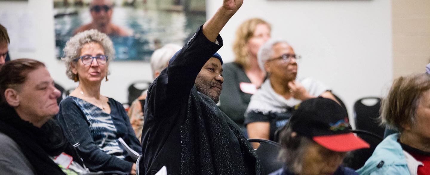 A black man raises his hand in a community forum