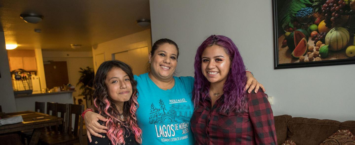a latinx mom and her two daughters smile in their home