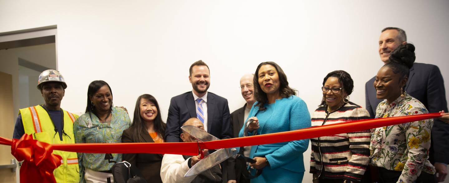 A multi-racial group including Mayor London Breed cut a red ribbon