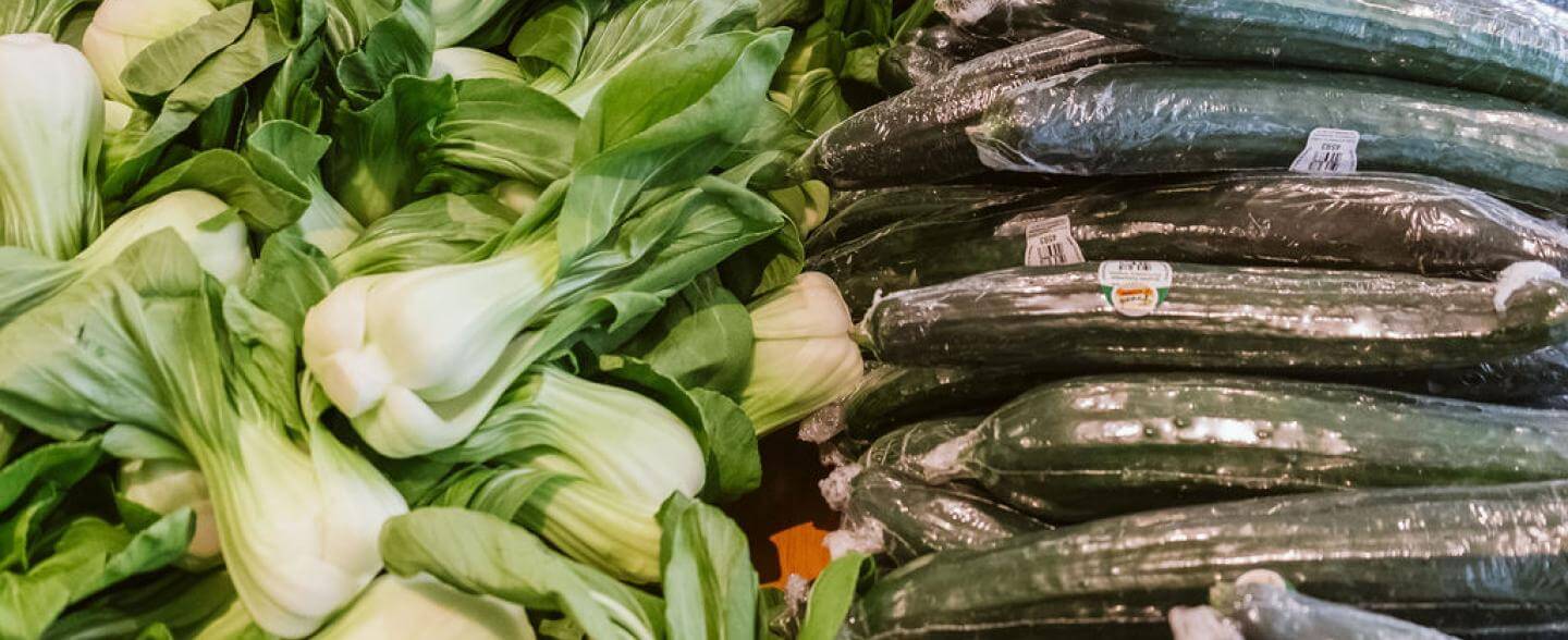 A pile of bok choy next to a pile of cucumbers