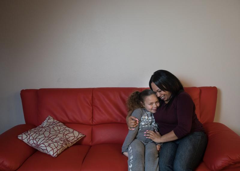 A Black mom happily hugs her child on a red couch