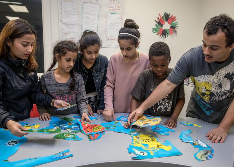 A multi-racial group of kids and teens work on a world map