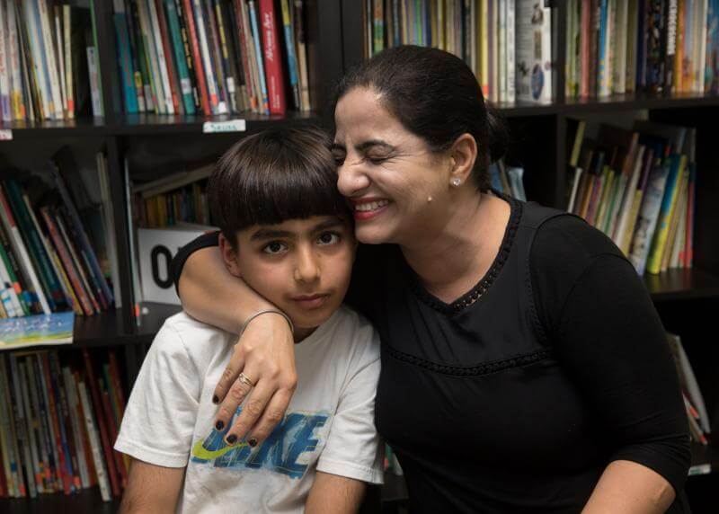 Mom squeezes her son in front of bookshelves