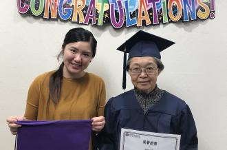 An Asian senior holds a graduation certificate with a staff-member 