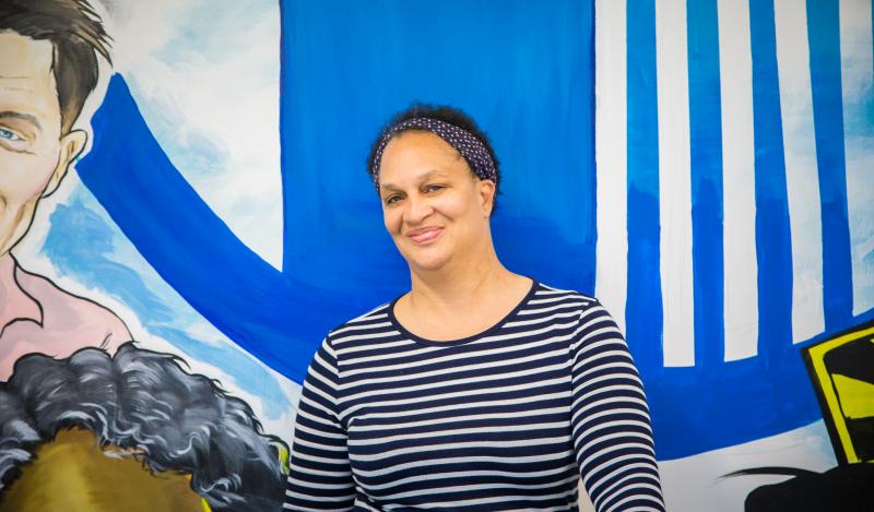 A black woman stands against a mural smiling