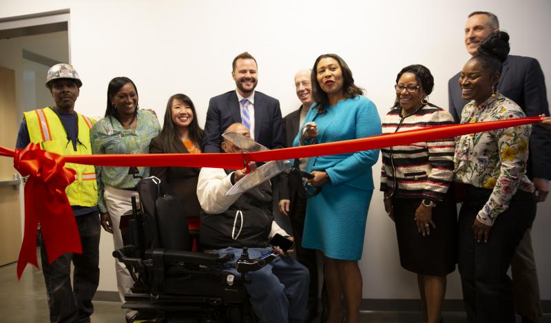 A multi-racial group including Mayor London Breed cut a bright red ribbon
