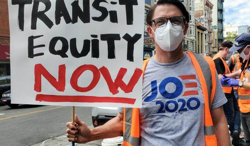 A TL Activist holds up a sign reading "Transit Equity Now"