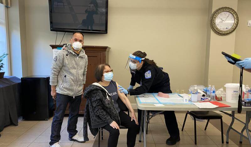 A senior tenant gets a shot from a medical professional, a social worker stands by