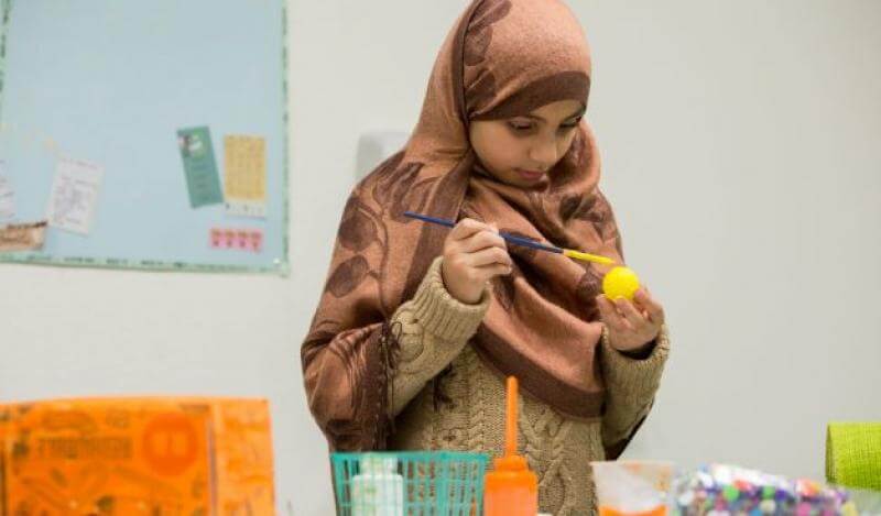 a young woman wearing a headscarf paints a ball yellow