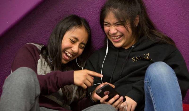 two young girls laugh while listening to music