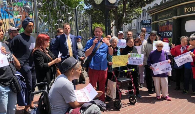 A diverse group of Tenderloin residents stand outside with safety protest signs