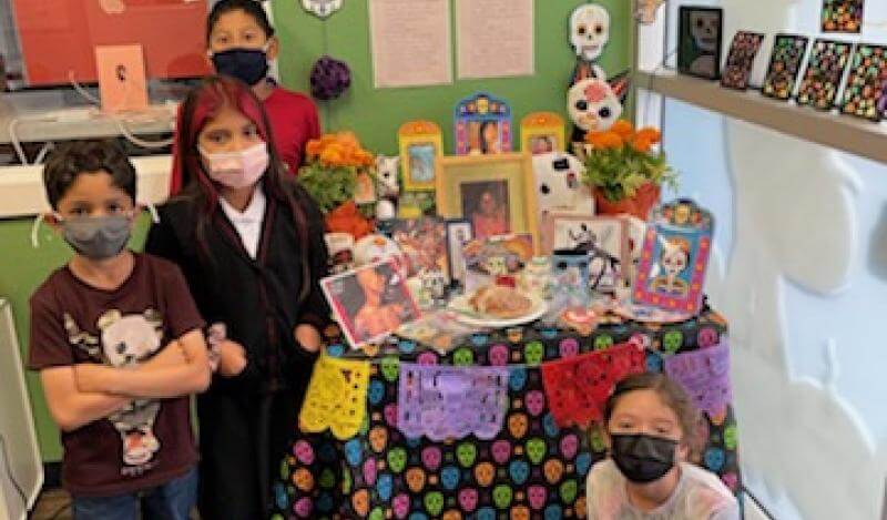 a group of kids stand in front of a dia de los muertos altar