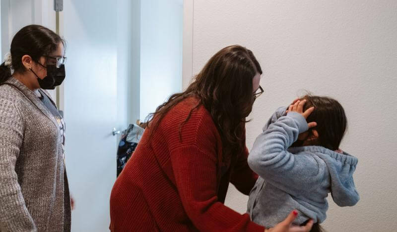 A mother helps her daughter put on her sweater