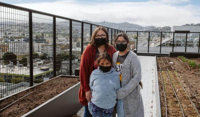 A mother and her two daughters stand on the rooftop of Casa Adelante -2828 16th Street