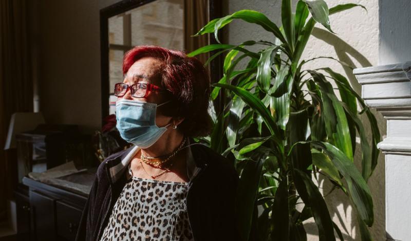 An older Filipina with red hair sits near a plant with light streaming on her face