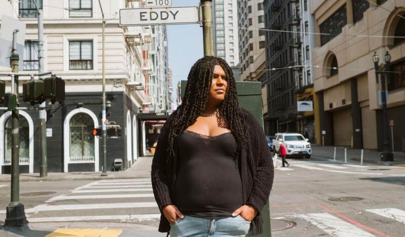 A woman in a black shirt stands outside against an Eddy Street sign