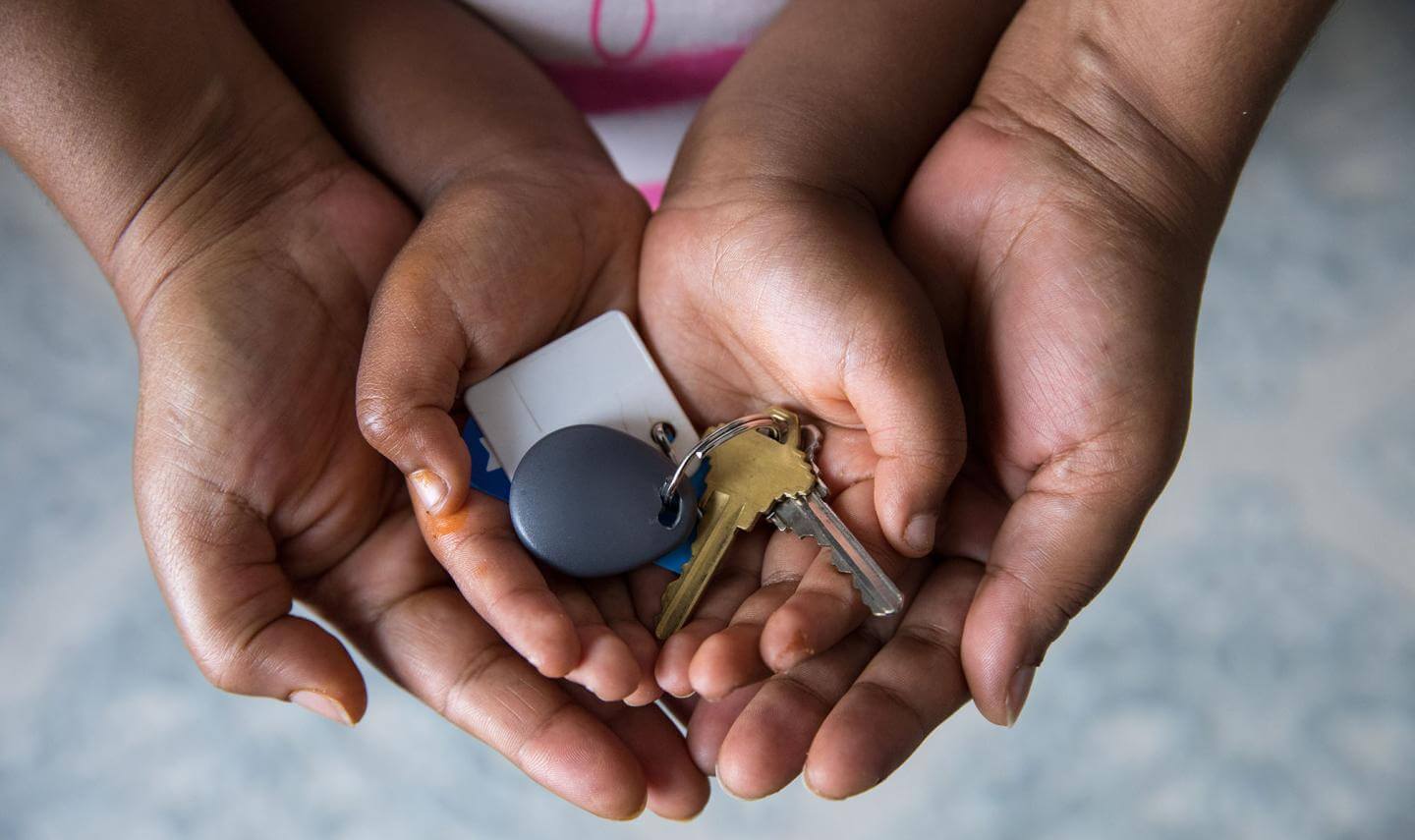 A Black mother's hands cradle child hands with house keys