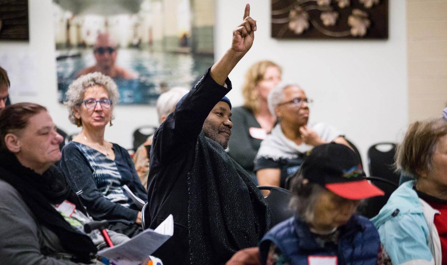 A black man raises his hand in a community forum