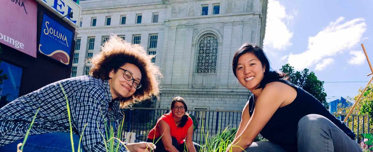 Three multi-racial females crouch down as they plant seeds in the Tenderloin People's Garden