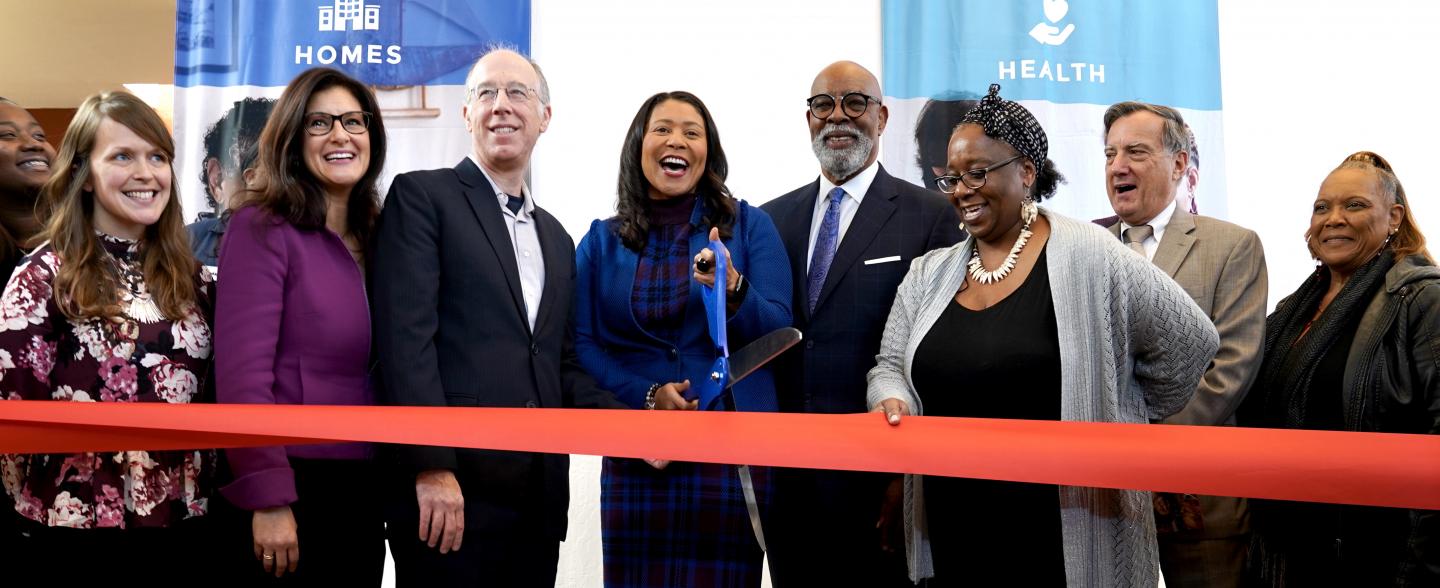 A multi-racial group including SF Mayor London Breed happily cut a red ribbon
