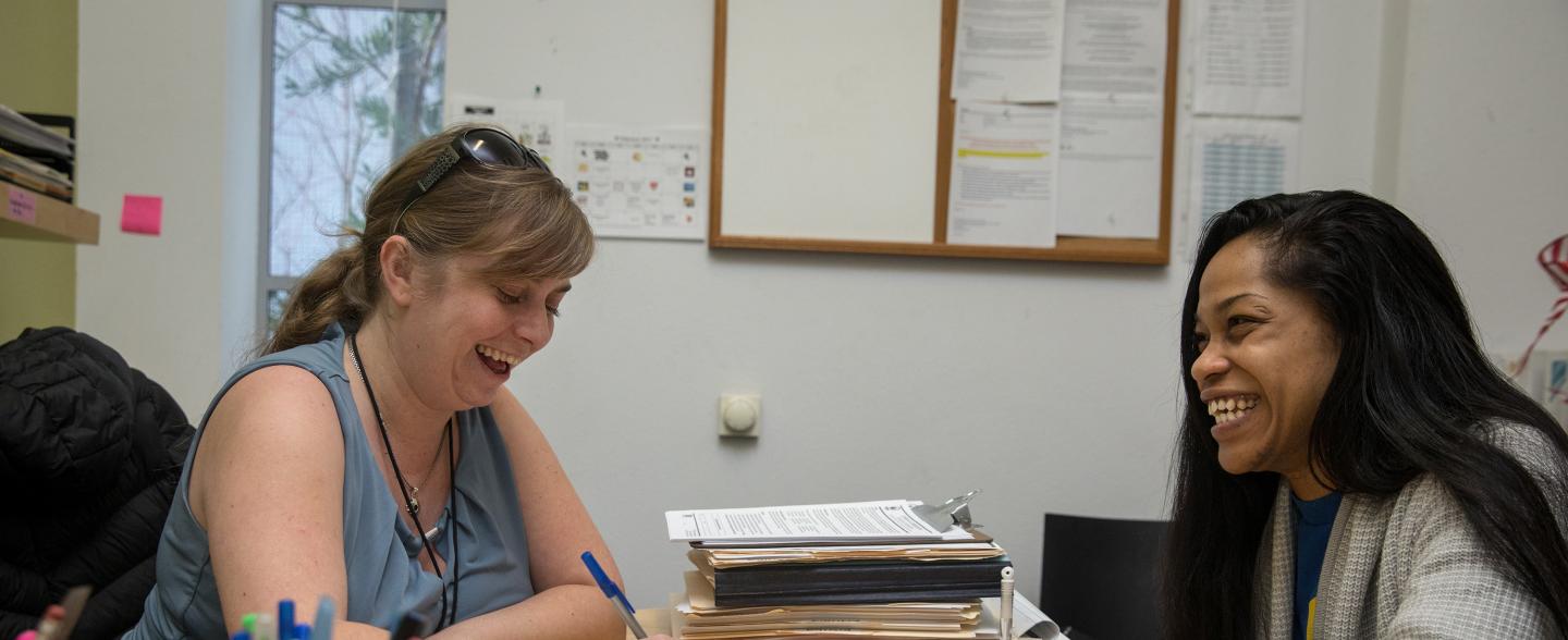 A white woman and black woman sit together in an office laughing