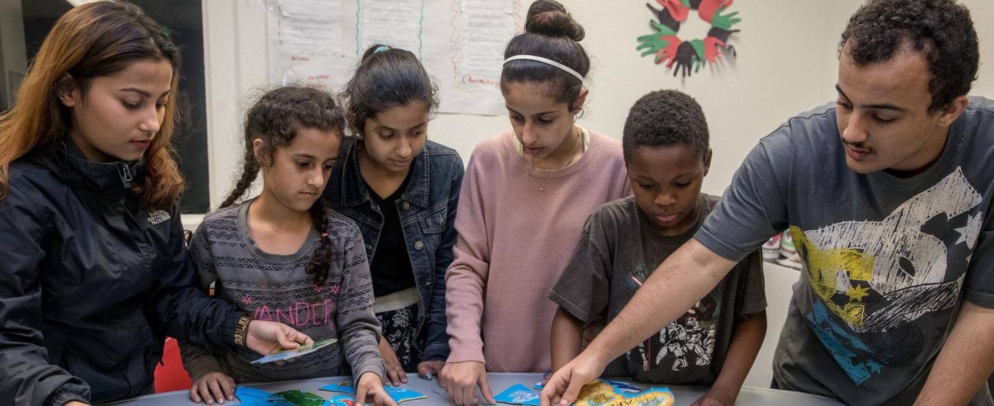 A multi-cultural group of kids and teens work on a map puzzle