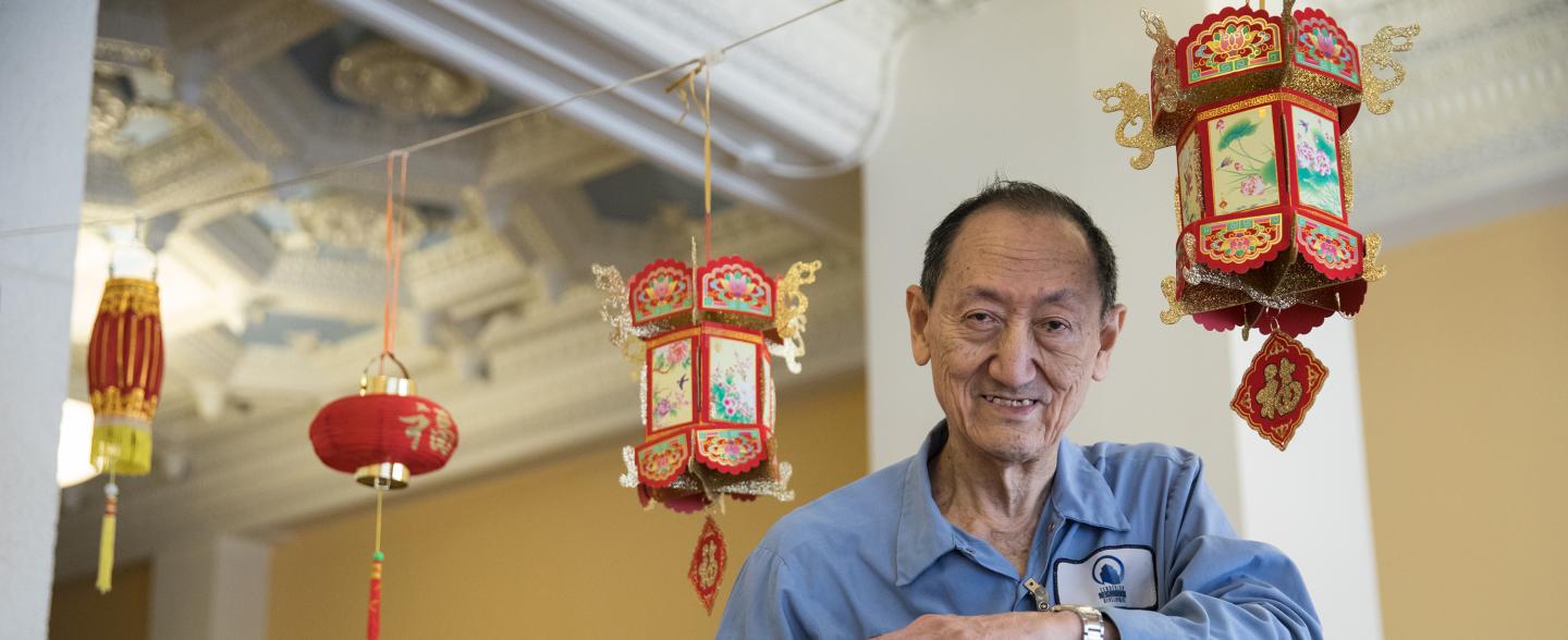 An Asian maintenance worker on a ladder smiles at the camera 