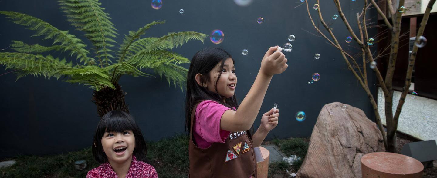 two asian-american sisters play with bubbles in a courtyard