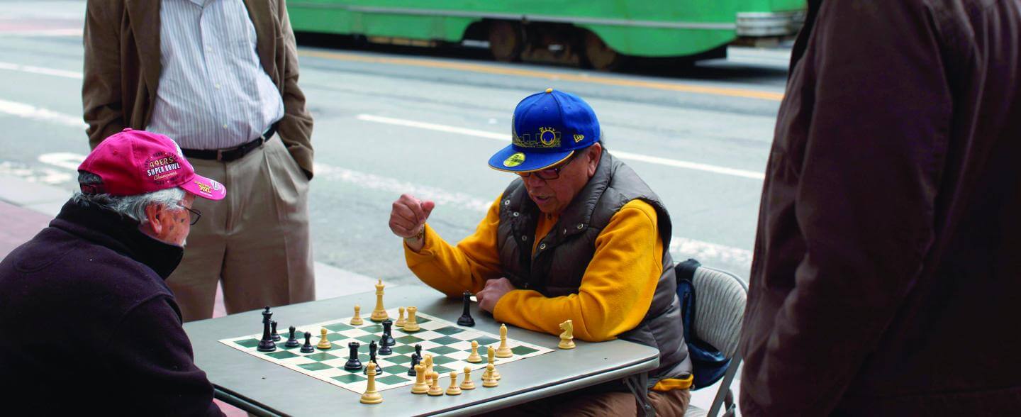 A multi-racial multi-generational group play chess outside