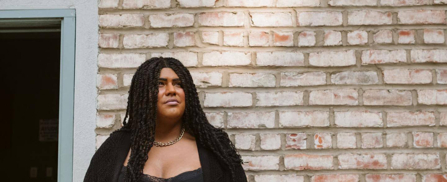 A woman in a black shirt stands in front of a brick wall looking upwards 