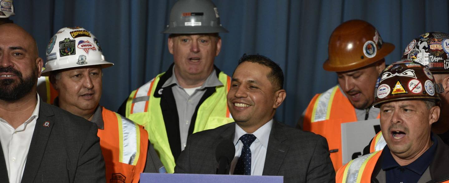 Maurilio León at a podium surrounded by people wearing hard hats