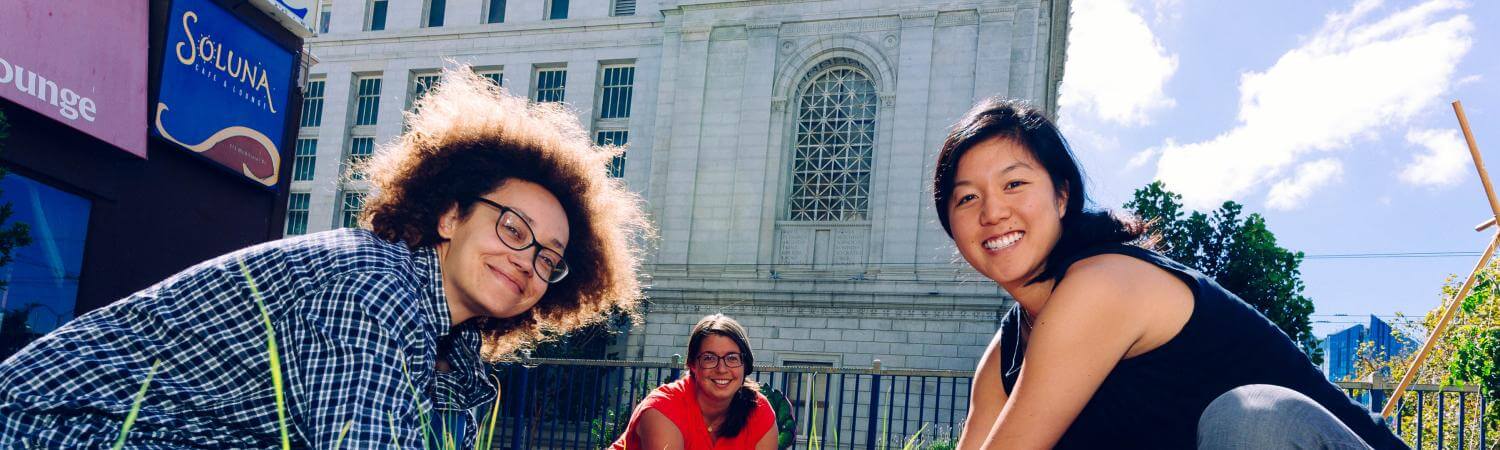 Three multi-racial females crouch down as they plant seeds in the Tenderloin People's Garden