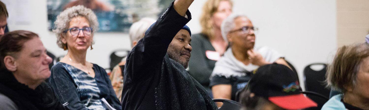 A black man raises his hand in a community forum
