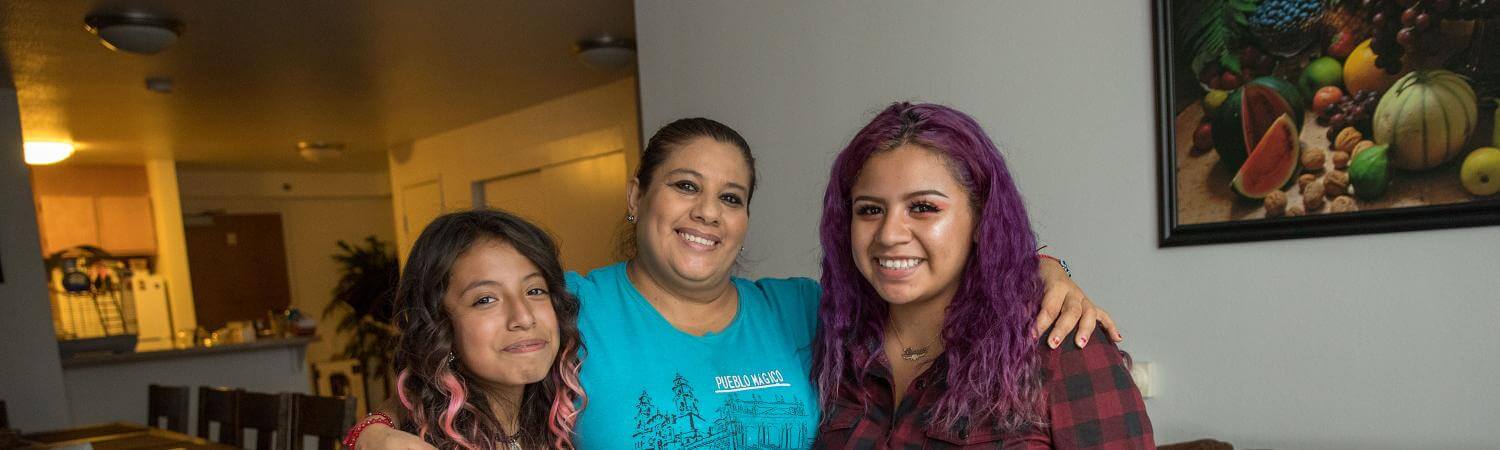 a latinx mom and her two daughters smile in their home