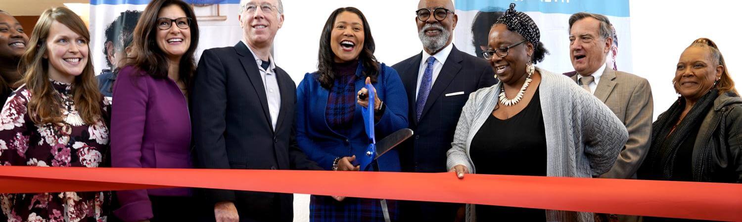 A multi-racial group including SF Mayor London Breed happily cut a red ribbon