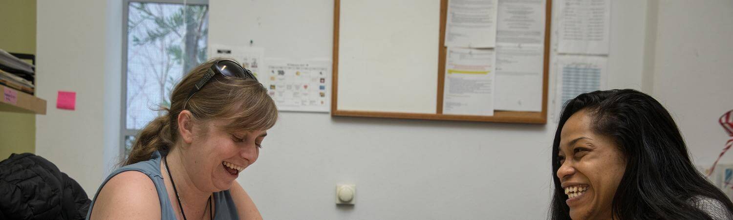 A white woman and black woman sit together in an office laughing
