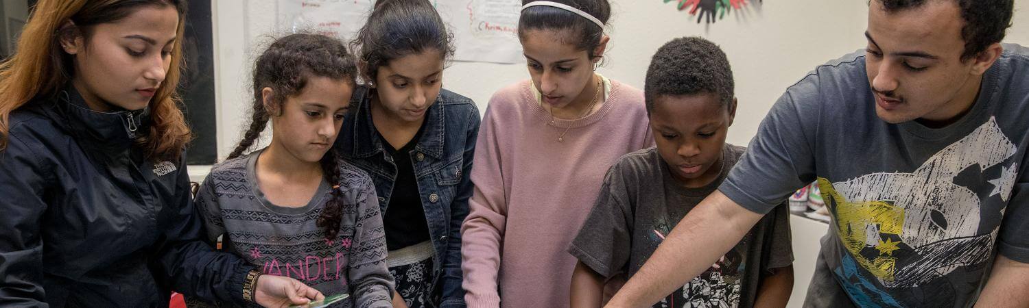A multi-cultural group of kids and teens work on a map puzzle