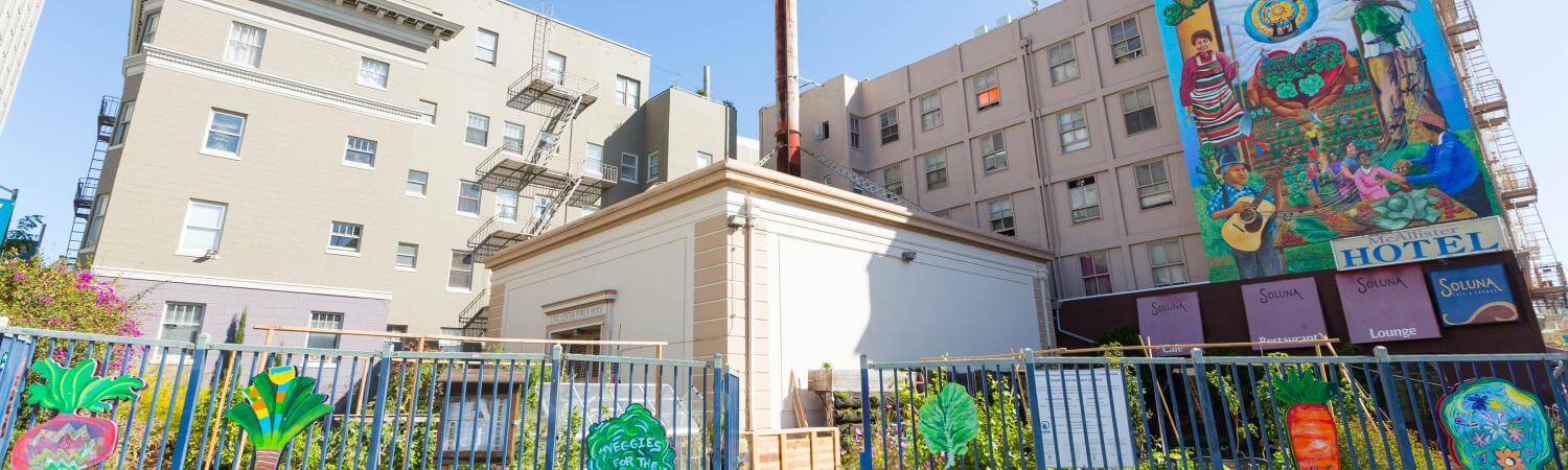 Front entrance to a large community garden with art on the fence and a vibrant mural 