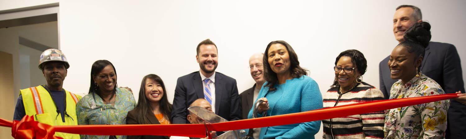 A multi-racial group including Mayor London Breed cut a red ribbon