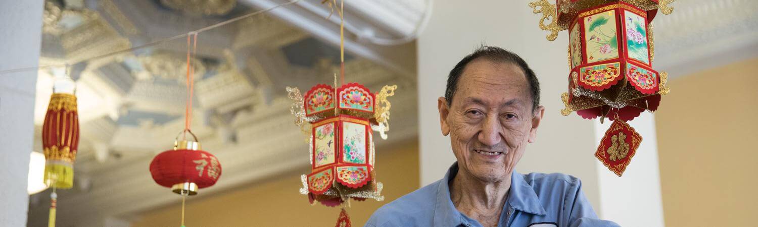 An Asian maintenance worker on a ladder smiles at the camera 