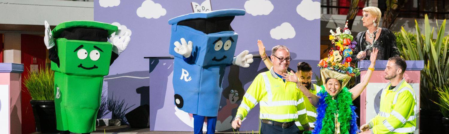 An Asian woman jumps out of recycling can on stage
