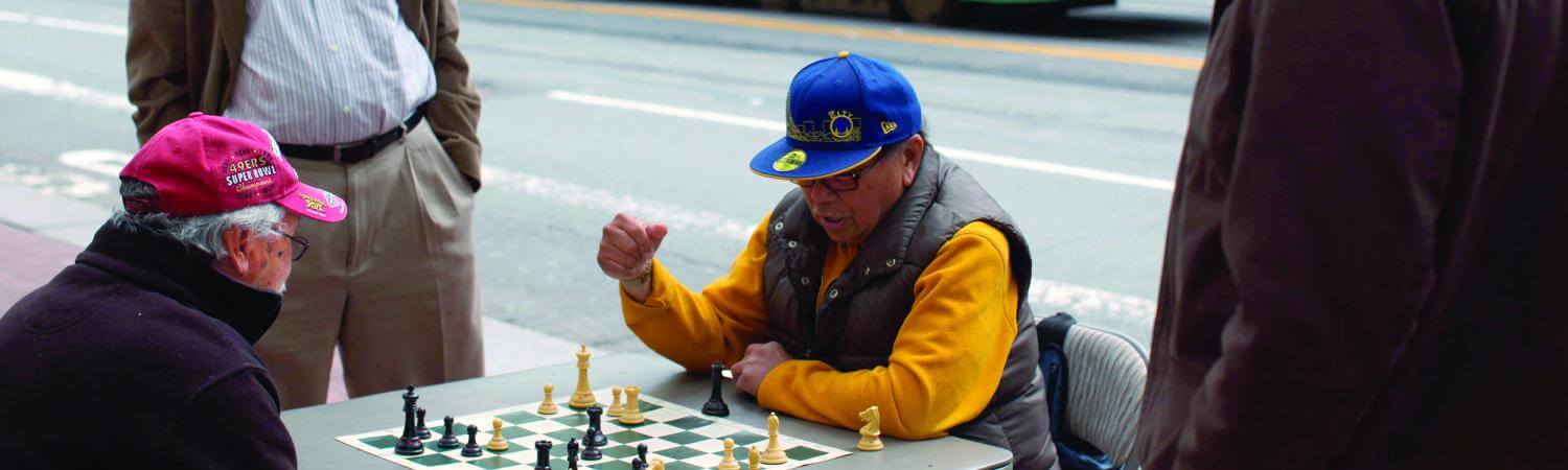 A multi-racial multi-generational group play chess outside