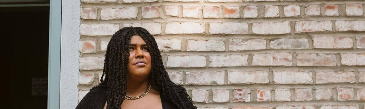 A woman in a black shirt stands in front of a brick wall looking upwards 