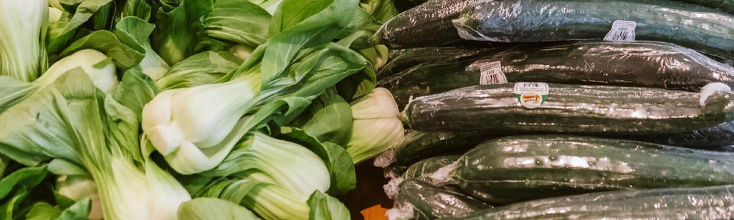A pile of bok choy next to a pile of cucumbers