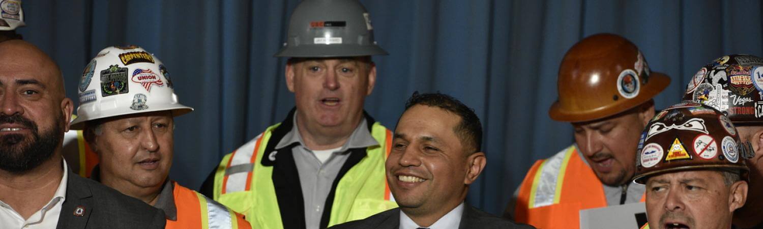 Maurilio León at a podium surrounded by people wearing hard hats