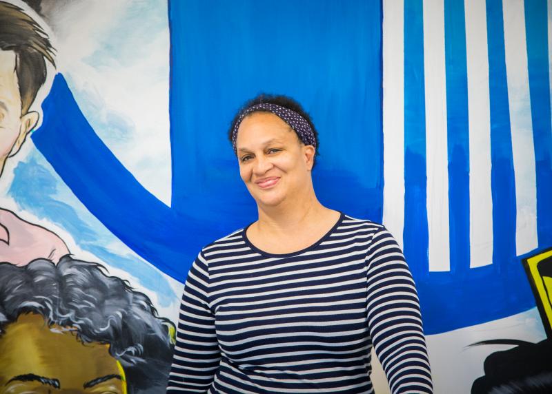 A black woman stands against a mural smiling