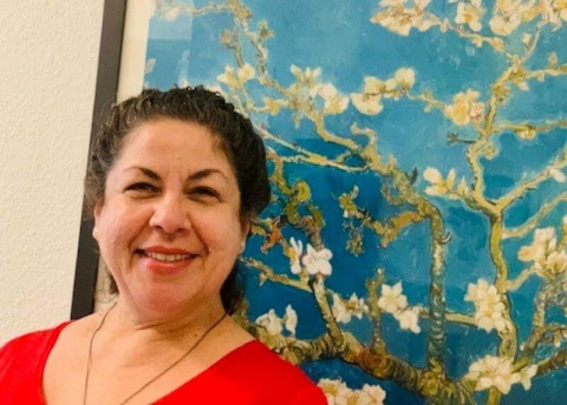 A latina with a bright smile poses in front of a painting