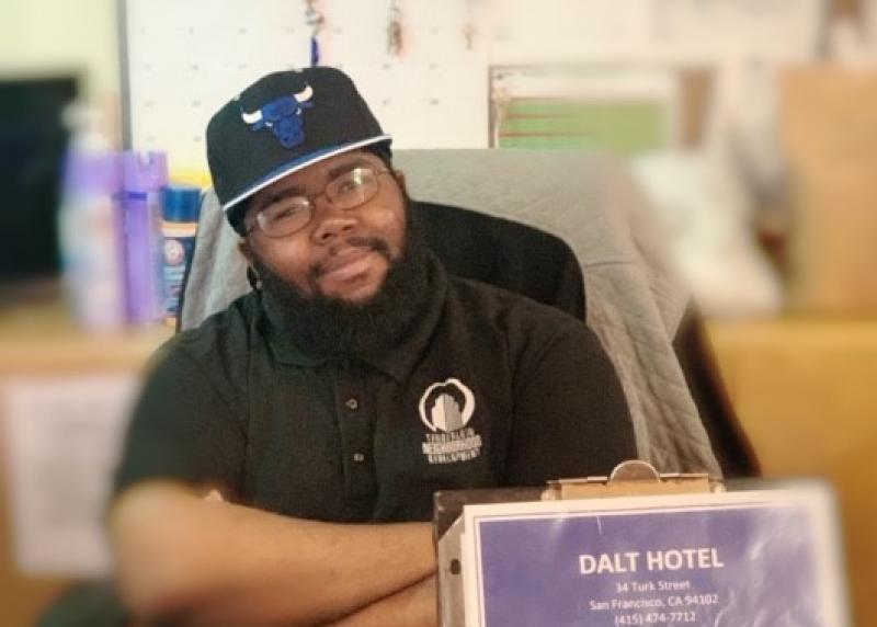 A young black man smiles at a front desk