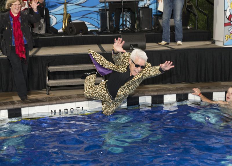 A white man in a cheetah suit flies over a pool 