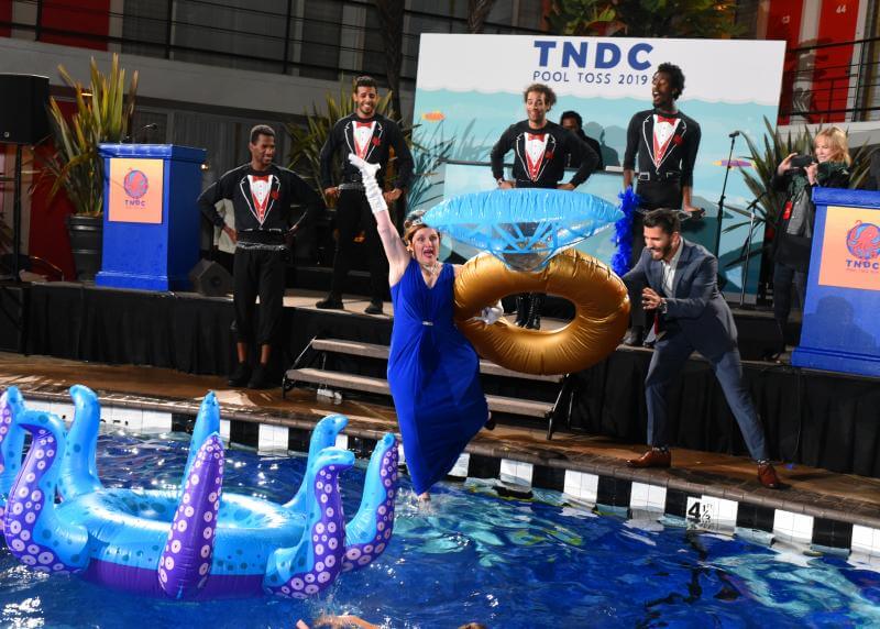 A white woman in a blue gown excitedly jumps into a pool